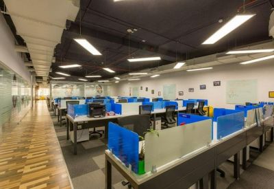 Rows of professional workstations with blue privacy dividers and overhead strip lighting.