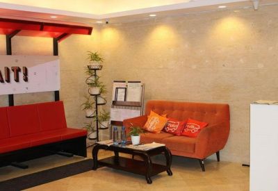 Reception area with an orange tufted sofa, a red bench, and potted plants on a tiered stand.