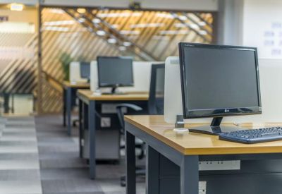 Open-plan office space with individual computer workstations and wooden desks.