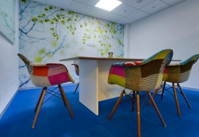 Small meeting room with bright blue flooring, patchwork upholstered chairs, and a nature-themed wall mural.