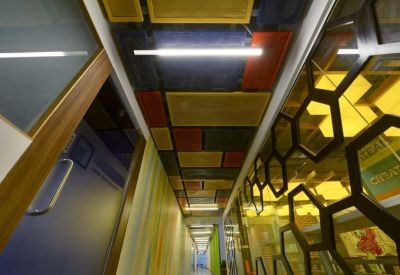 Narrow office corridor featuring a vibrant, multicolored paneled ceiling and glass partitions with honeycomb patterns.