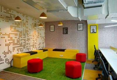 Vibrant breakout area with green turf flooring, yellow bench seating, and red ottomans.