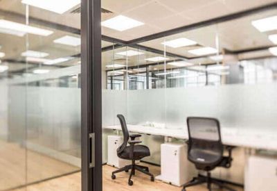 Bright workspace featuring white desks and black ergonomic chairs behind glass partitions.