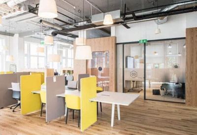 Vibrant coworking area with yellow privacy screens, wooden flooring, and industrial-style exposed ceilings.