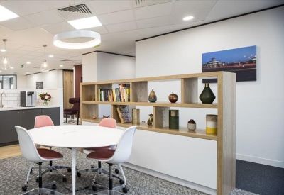 Bright breakout area with a round white table, pink-accented chairs, and a wooden bookshelf.