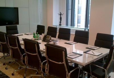 Modern boardroom featuring a long white table, black leather chairs, and a large wall-mounted screen.