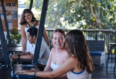 Coworking members collaborating at a wooden table on a shaded outdoor terrace.