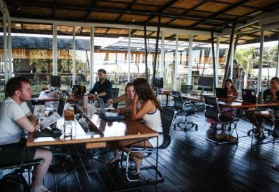 Spacious open-plan workspace featuring industrial-style wooden desks and large glass walls.