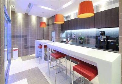 Communal kitchen area featuring a white breakfast bar, red stools, and orange pendant lights.