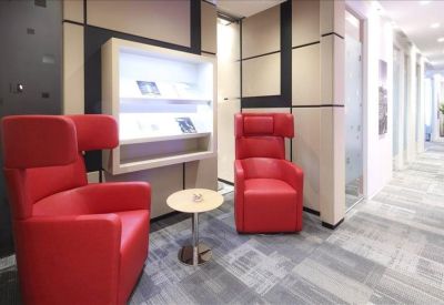 Reception lounge with vibrant red wingback armchairs and a built-in display shelf.