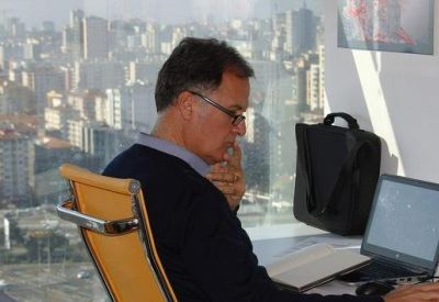 Close-up of a professional at a desk with a laptop and panoramic city views through large windows.