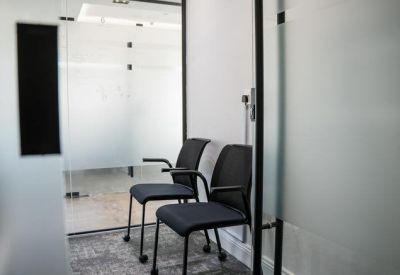 Two black fabric chairs in a bright hallway waiting area next to frosted glass walls.