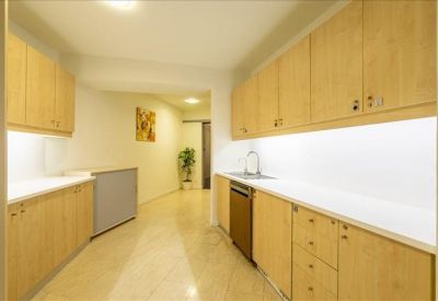 Modern office kitchen with light wood cabinetry and long white countertops.