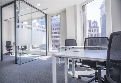 Bright open-plan office area with white desks and large windows overlooking the city.