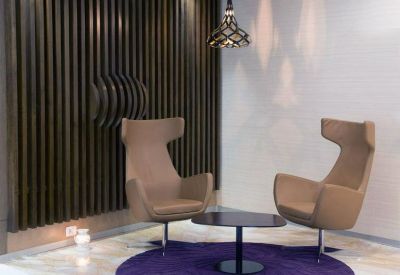 Stylish lounge area with tan wingback chairs, a purple rug, and a wood-slat feature wall.