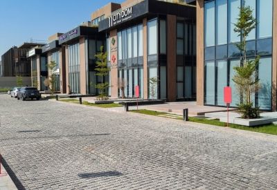 Paved entrance courtyard alongside glass-fronted office suites and young trees.