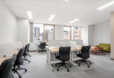 Open coworking space with desks, black office chairs, and a colorful lounge area by the window.