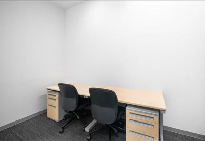 Small private office with two desks and ergonomic chairs against a white wall.