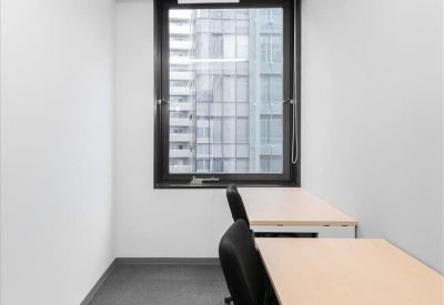 Narrow private two-person office suite with light wood desks and a city view window.