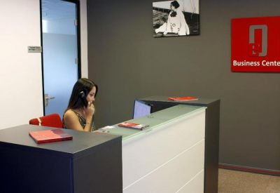 Modern reception desk with a white front and a dark countertop, featuring a wall-mounted business logo.