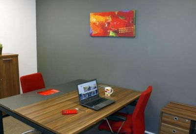 Bright private office featuring a wooden desk, two red chairs, and a vibrant red and yellow abstract painting.