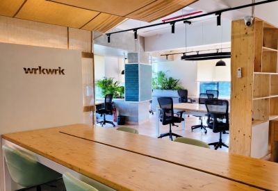 Open-plan coworking area with light wood desks, ergonomic chairs, and indoor plants.