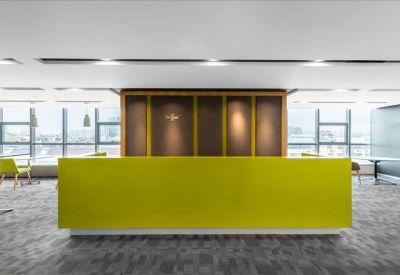 Minimalist reception desk in a bright yellow finish against a wood-paneled wall.