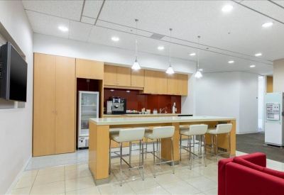 Office kitchen area and breakroom with a high wooden bar table and white stools.