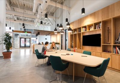 Large shared workspace featuring a long wooden table, green seating, and industrial ceiling details.