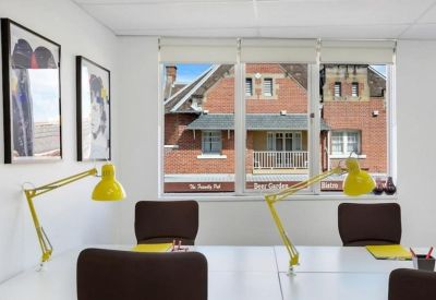 Sunlit workspace with yellow desk lamps and views of brick buildings through large windows.