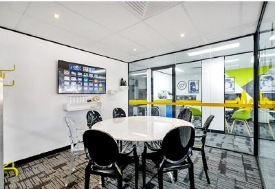 Bright glass-walled meeting room with a round table and black designer chairs.