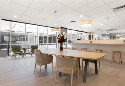 Modern communal break area with a large wooden table and green armchairs.