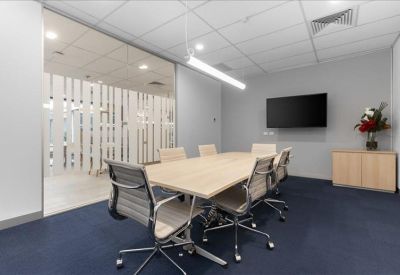 Professional meeting room featuring a long wooden table and wall-mounted screen.