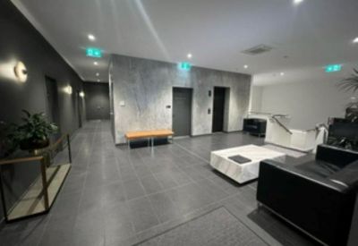 Modern building lobby with grey tiled floors and a black leather sofa.