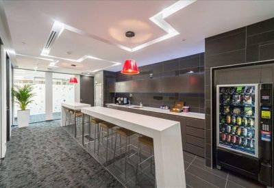 Sleek communal kitchen and breakout area with white breakfast bar and vending machine.