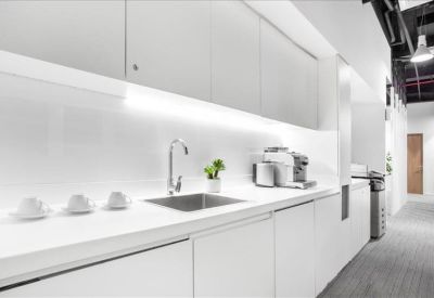 Sleek all-white office kitchenette with built-in cabinetry and coffee making facilities.