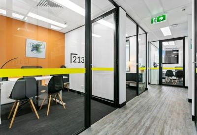 Private glass-walled office with black chairs and an orange feature wall.