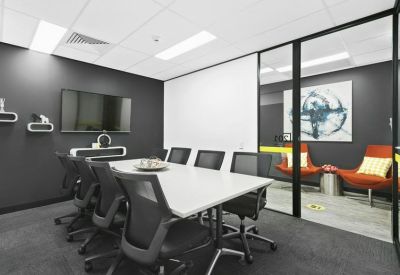 Modern conference room with a large white table, black mesh chairs, and a screen.