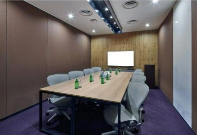 Professional boardroom with a long wooden table, grey ergonomic chairs, and a wall-mounted screen.