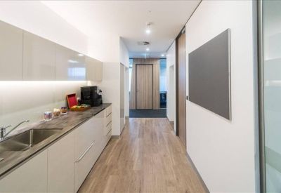 Modern office kitchen and breakout area with sleek white cabinetry and wooden flooring.