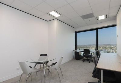 Small internal office with a round glass meeting table and a corner desk facing the window.