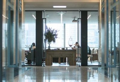 Bright hallway leading to an office space with glass partitions and city views.
