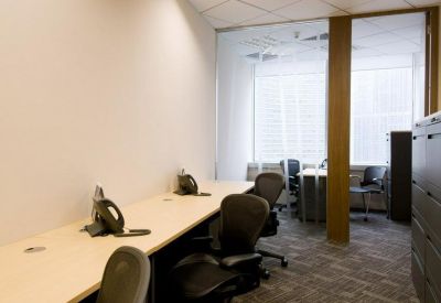 Shared office workspace with long desks, ergonomic black chairs, and a glass-walled private office.