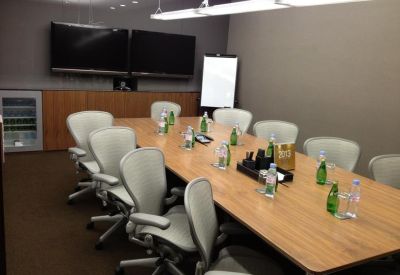 Large boardroom with a long wood-finish table, ergonomic grey chairs, and dual video conferencing screens.