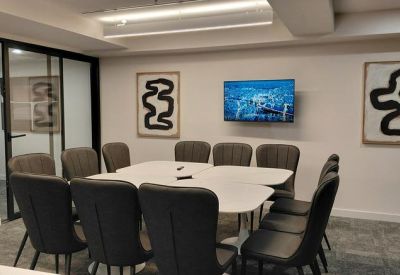 Modern conference room with white tables, grey chairs, and a wall-mounted TV.