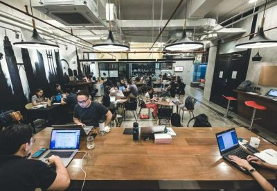 Open-plan workspace with long wooden desks, hanging pendant lights, and wall murals.