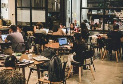 Busy coworking space with people working at round wooden tables.