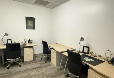 Small three-person office with light wood desks and black ergonomic chairs.