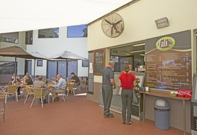 On-site outdoor café with a service counter, menu board, and patrons seated under umbrellas.