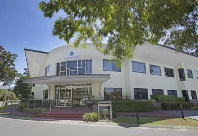 Entrance to the building featuring a curved facade, glass doors, and manicured landscaping.